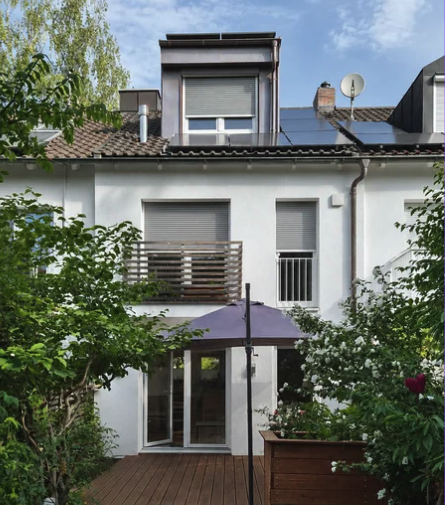 Reihenhaus in München-Obergiesing nach der Sanierung: weiß gedämmte Fassade, neue Dachgaube, PV-Anlage auf dem Dach und Holzterrasse